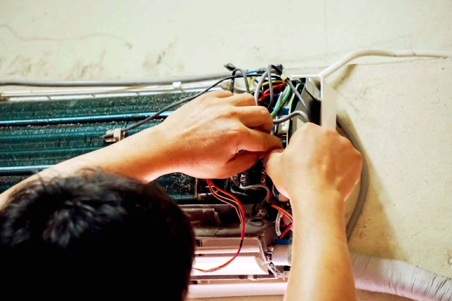 A person working on wires in front of an air conditioner.